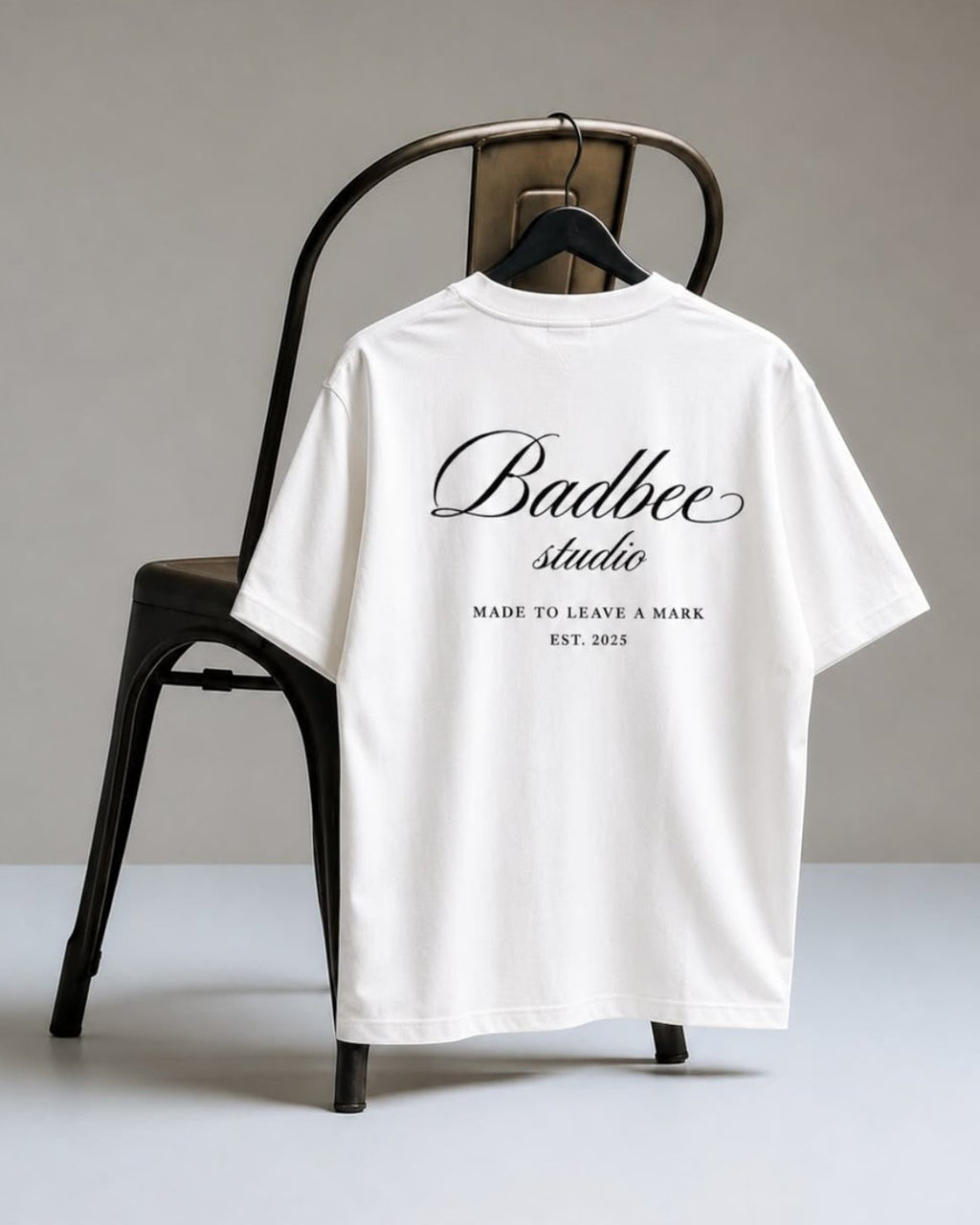 Hoodies Liban white oversized Turkish cotton t-shirt with black Badbee studio logo print on the back hanging on a chair