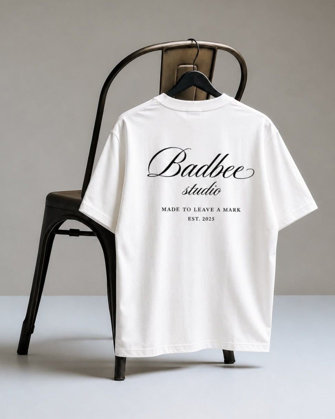Hoodies Liban white oversized Turkish cotton t-shirt with black Badbee studio logo print on the back hanging on a chair